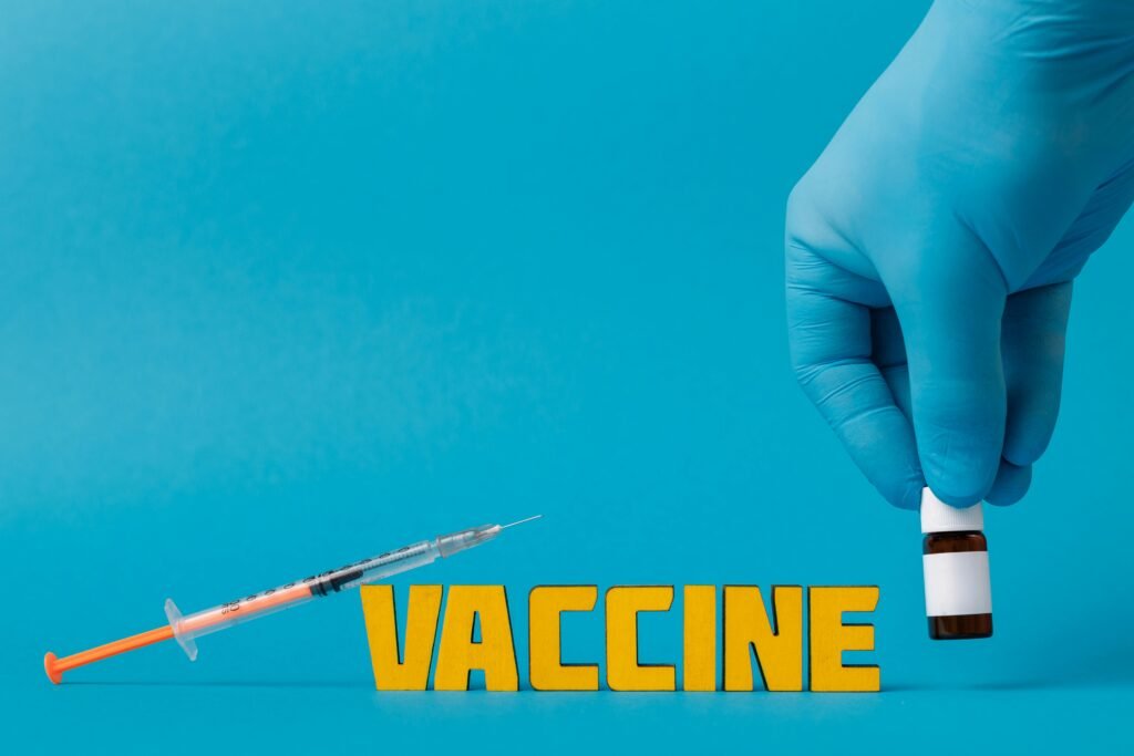 An image of a healthcare worker who put on PPE (gloves), holding vaccine bottle with syringe in a blue background.