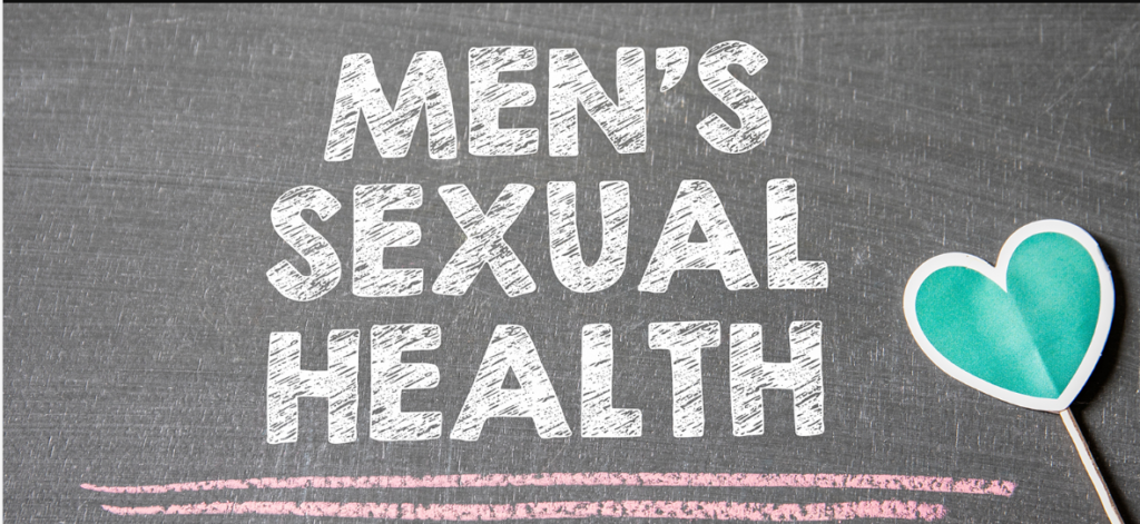 This image features the phrase "Men's Sexual Health" boldly displayed in white, chalk-like letters on a dark grey chalkboard background. Beneath the words, there's a soft pink chalk line adding a touch of warmth. To the right, a cheerful turquoise heart on a stick — almost like a playful paper cutout — gently balances the serious tone with a hint of care and positivity. The image exudes an approachable and informative quality, emphasizing the importance of men's sexual health in a way that blends education with compassion and openness.